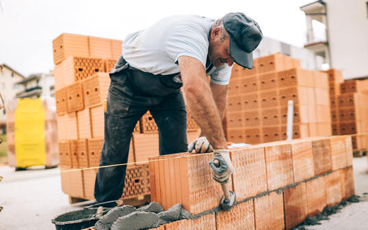 industrial worker building exterior walls, using hammer for laying bricks in cement. Detail of worker with tools and concrete