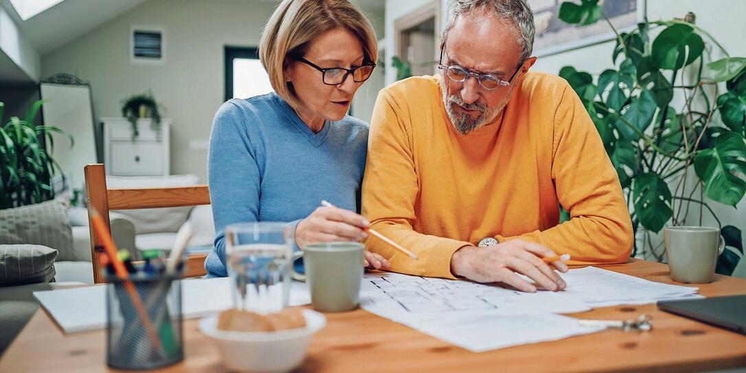 Senior couple sitting at table and looking into blueprints of their new home