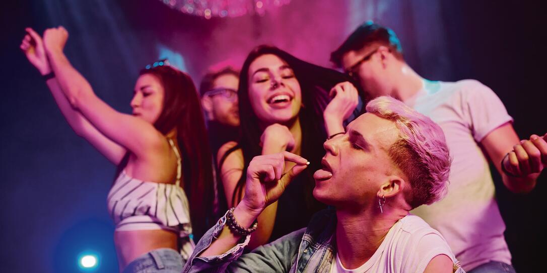 Guy taking drug pill. Young people is having fun in night club with colorful laser lights