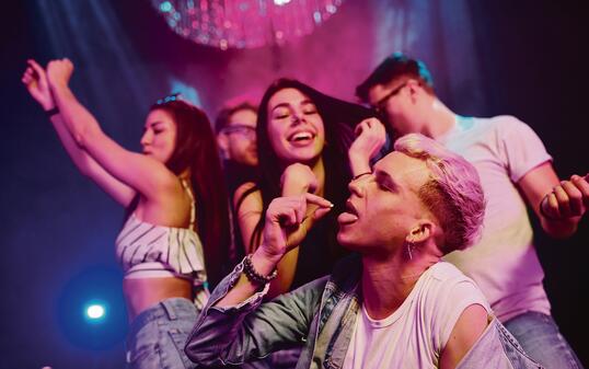 Guy taking drug pill. Young people is having fun in night club with colorful laser lights