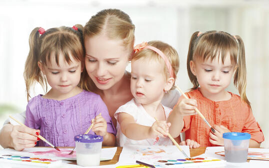 children twin sisters draw paints with her mother in kindergarten