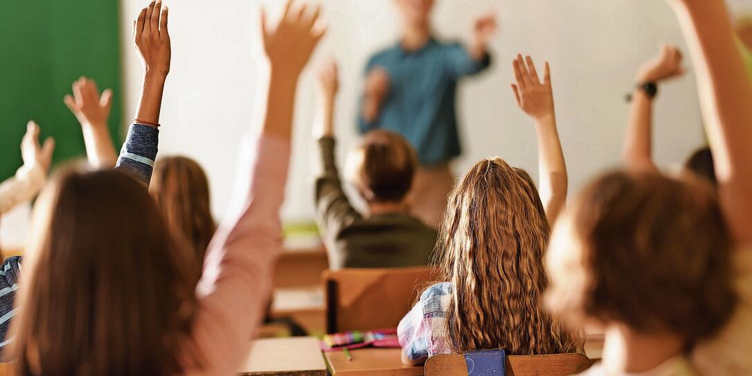 Back view of school kids raising their hands on a class in the classroom.