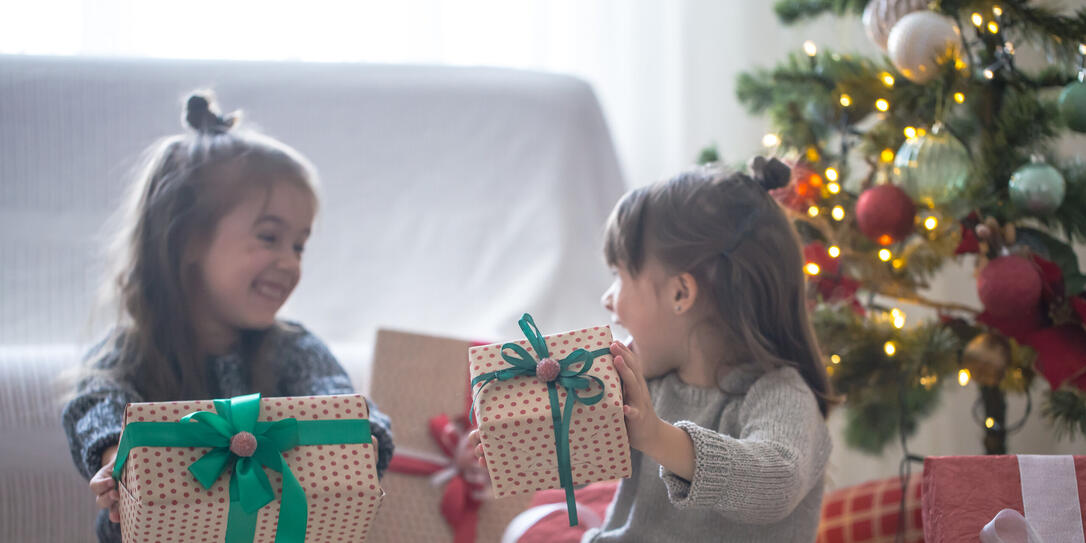 Pretty little girls are holding a gift boxes and smiling at home on light background