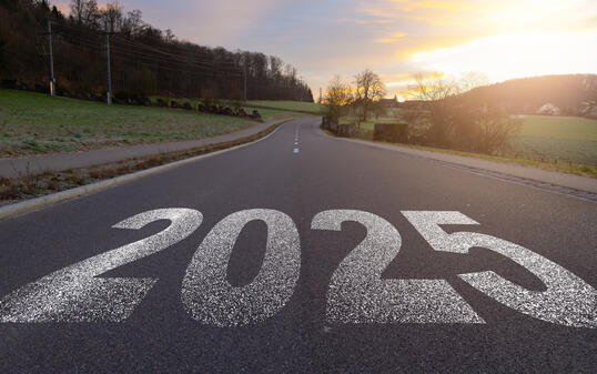 The word 2025 written on highway road in the middle of empty asphalt road at golden sunset and beautiful blue sky. Concept for year 2025.