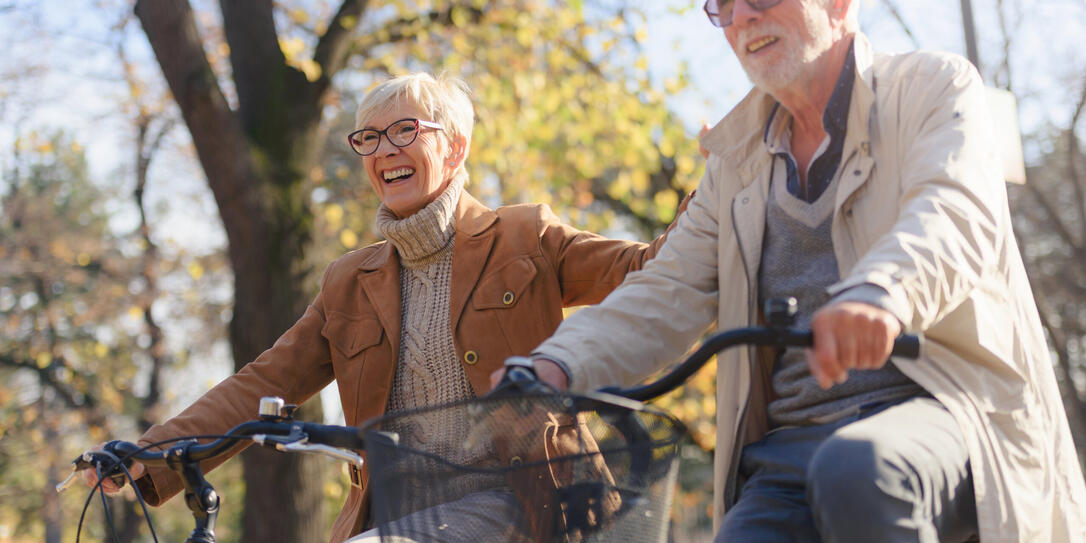 Cheerful active senior couple with bicycle in public park together having fun