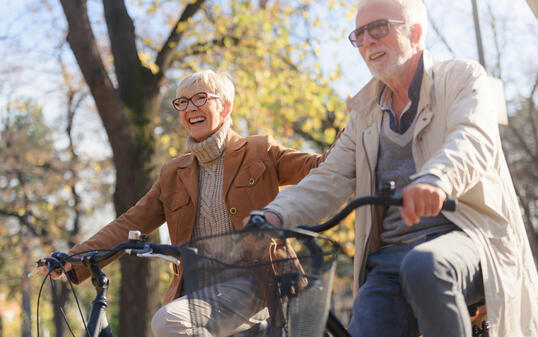 Cheerful active senior couple with bicycle in public park together having fun