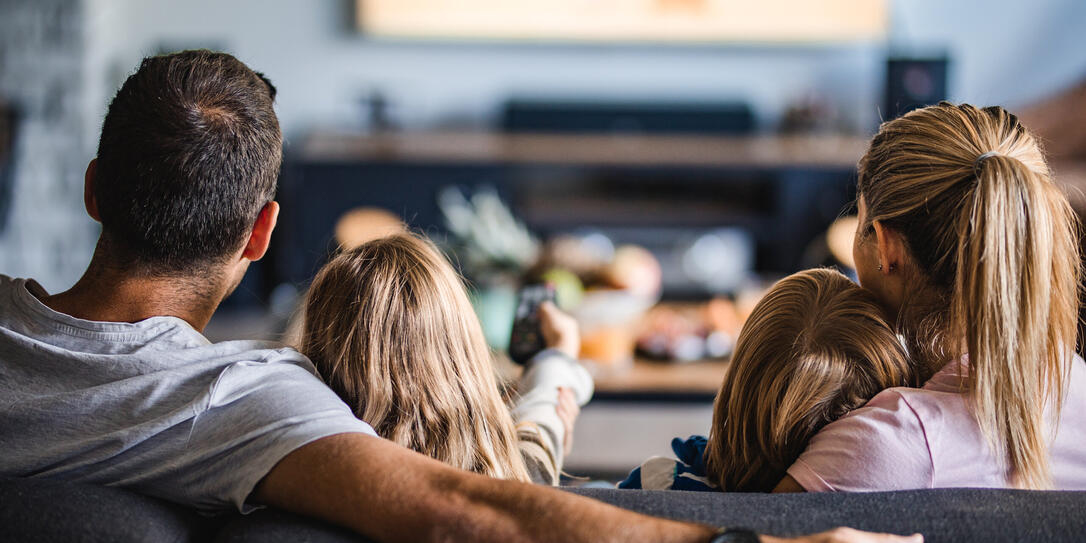 Rear view of a family watching TV on sofa at home.